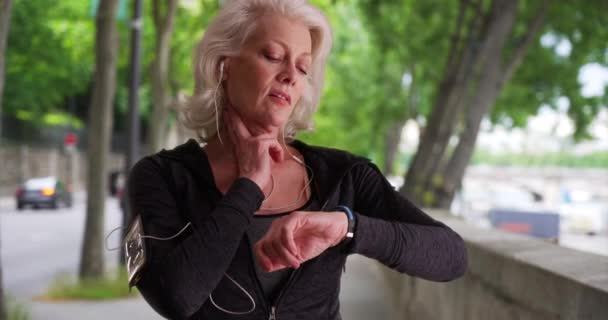 Зрелая Бегунья Проверяет Пульс Здоровая Активная Женщина Слушает Музыку Телефоне — стоковое видео
