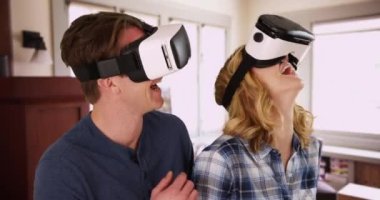 Evde akıllı telefon VR kulaklığı kullanan erkek ve kadın portresi, etrafa bakıyor ve işaret ediyor. İki arkadaş sanal gerçekliği tecrübe ederek eğleniyor, içerde gülüyor ve gülüyorlar. 4k