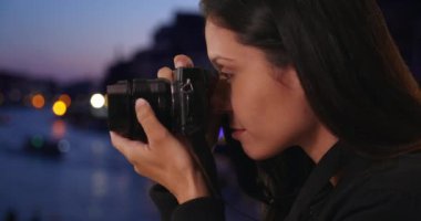 Gece Grand Canal 'da DSR kamerasıyla fotoğraf çeken turist kadının yan görüntüsü. İtalya 'da milenyum dişisi objektife odaklanıyor ve tarihi şehirde akşam fotoğrafı çekiyor. 4k