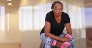 Yaşlı siyah bir kadın ağırlık kaldırdıktan sonra bir portre için poz verir. Yaşlı bir Afrikalı Amerikalı kadın spor yaptıktan sonra kameraya bakar. 4k