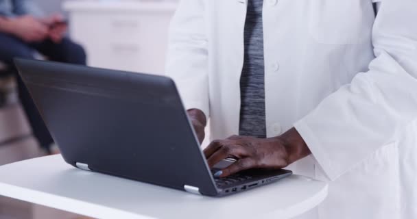 ポータブルコンピュータ室内クリニックに入力している黒い医師の閉鎖 ラップトップコンピュータとアフリカの上級医師のタイプのタイトなショット — ストック動画