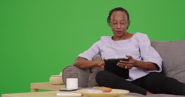 Starsza Czarna Kobieta Używa Tabletu Relaksując Się Kanapie Zielonym Ekranie — Wideo stockowe
