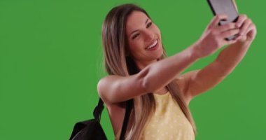 Mutlu gülümseyen Millennial kadını yeşil ekranda akıllı telefonuyla selfie çekiyor. 20 'li yaşlarda beyaz bir kız cep telefonuyla fotoğraf çekiyor. Tuşlama veya birleştirme için yeşil üzerine 4K