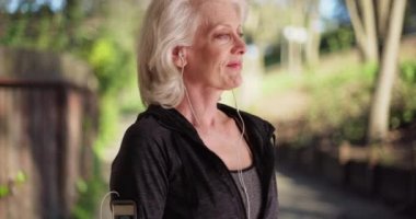 Neşeli koşucu, akıllı saati kullanarak güneşli parkta kameraya gülümsüyor. Koşudan sonra dışarıda kameraya gülümseyen kulaklık takan olgun bir kadın. 4k