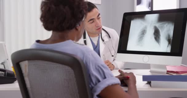 老年非洲病人去看医生 检查肺部X光检查结果 年轻的西班牙放射学家用计算机向非洲老年妇女展示了她的肺X光照片 — 图库视频影像