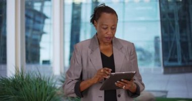 Ofis binasının dışında dijital tablet kullanan Afro-Amerikan kadın. Yaşlı siyahi iş kadını dokunmatik ekran bilgisayar kullanıyor. 4k
