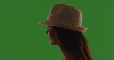 Yeşil perdenin önünde fötr şapka takan çekici genç bir kadının silueti. Profil görüntüsü: Şapkalı ve saçı yeşil ekranda uçuşan güzel bir bayan. 4k