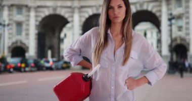 Milenyum kızı, Londra, İngiltere 'de Amiral Kemeri' nin kalçalarına kırmızı gaz konteynırı tutarak poz veriyor. Benzine ihtiyacı olan genç beyaz bir kadın Londra caddesinde kameraya bakıyor. 4k