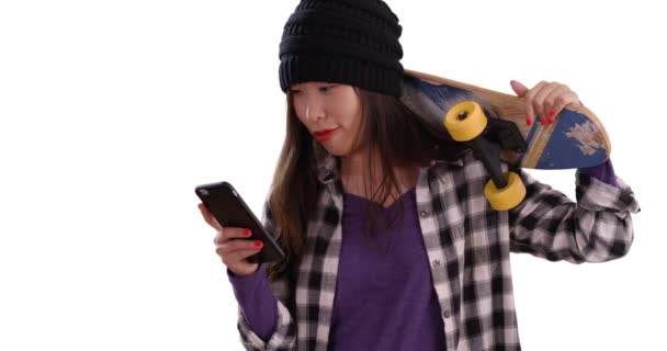 嬉皮士千禧年的女人使用智能手机 肩膀上架着滑板复制空间 一个年轻的亚洲女人拿着一块被白色背景隔离的滑板自拍的肖像 — 图库视频影像