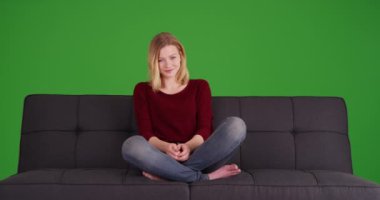 Kanepede oturan, gülümseyen ve yeşil ekranda kameraya bakan sıradan sarışın kadın. Anahtar ya da birleşik olmak üzere yeşil ekranda.