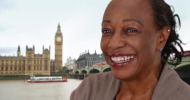 Londra 'da kameraya gülümseyen ve gülen tatlı olgun bir kadın. Big Ben saat kulesinin yanındaki Afrikalı Amerikalı kadının gülümseyen portresi. 4k