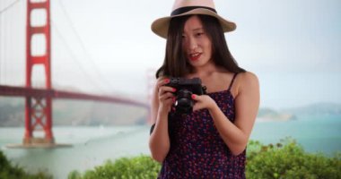 Golden Gate Köprüsü 'nün önünde kamerayla fotoğraf çeken güzel bir fotoğrafçının portresi. San Francisco California 'da fotoğraf çeken Asyalı genç bir kadının yakın görüntüsü. 4k