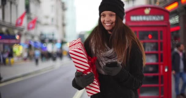 Mujer Joven Sosteniendo Regalo Navidad Teléfono Inteligente Mirando Alrededor Sonriendo — Vídeo de stock