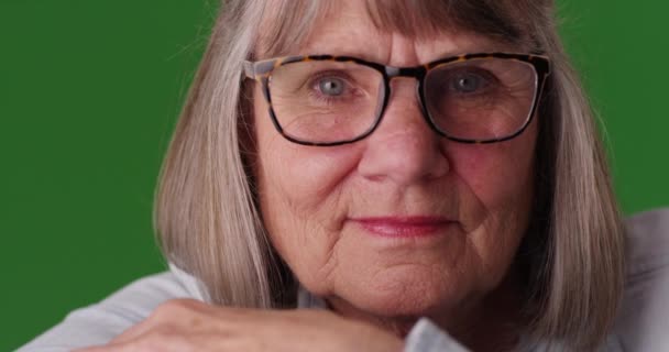 緑の画面の前に眼鏡をかけた老女のクローズアップ 緑の画面上のカメラを見てリラックスしたシニア女性の顔を間近で見ることができます — ストック動画