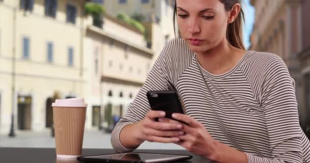 在意大利城市 一位年轻的女士坐在咖啡桌旁 一边发短信一边打电话 在外面的意大利咖啡店里 一个白人女人在智能手机上用咖啡聊天 — 图库视频影像