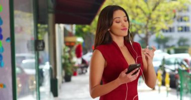 Tatlı Latin bir bayan cep telefonuyla müzik dinliyor ve yaz günü ritmle dans ediyor. Kadın, şehir merkezindeki bir sokakta, kamera önünde flört ederek el sallıyor. 4k