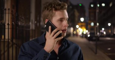 Şehir sokağında müşteriyle telefonda konuşan yakışıklı iş adamının portresi. Geceleri dışarıda cep telefonuyla konuşan mutlu beyaz erkek. 4k