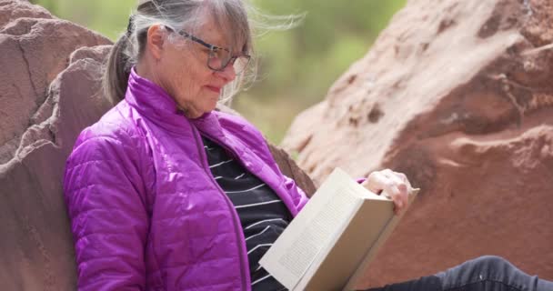 这张特写是快乐的老年女性在户外看书和喝咖啡的特写 成熟的户外爱好者笑着 坐在岩石旁边看书 — 图库视频影像
