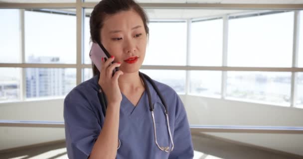 工作的千年护士穿着洗浴服 在办公室诊所内使用移动设备 严肃的年轻亚洲医生在空荡荡的医院里用手机交谈 — 图库视频影像