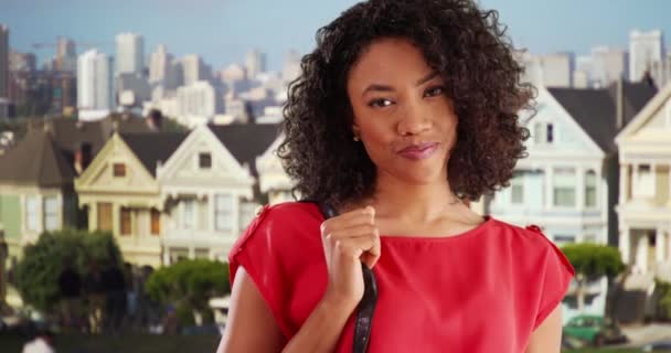 美丽的非洲女性站在旧金山的住宅区 对着镜头微笑 红色的顶部是可爱的游客的画像 背景是城市景观 — 图库视频影像