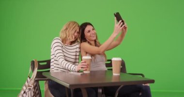 Güzel beyaz kızlar cep telefonuyla selfie çekmek için yeşil ekrandaki tablette poz veriyorlar. Krom anahtar bileşimi için akıllı telefonlu iki çekici genç kadın selfie çekiyor. 4k
