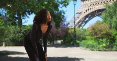 Paris 'te soluklanmak için mola veren zenci bir sporcu kadın. Aktif haldeki kadın koşucu dinleniyor ve bacağını esnetiyor. 4k