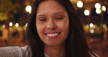 Milenyum kadınının POV 'u gece şehir sokaklarında cep telefonuyla selfie çekiyor. Şehir ortamında Bokeh ışıkları olan güzel bir kadının akıllı telefon ekranından görüntüsü. 4k