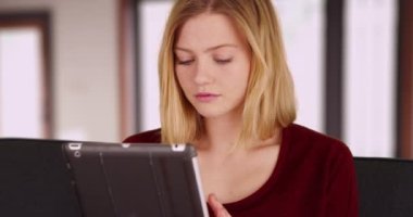 Evinde teknolojiyi kullanarak rahatlamış sevimli bin yıllık kadın portresi. Kanepede dijital tablette kitap okuyan otantik beyaz bir kadın. 4k