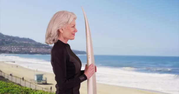 Профиль Привлекательной Пожилой Женщины Держащей Доску Серфинга Смотрящей Океанские Волны — стоковое видео