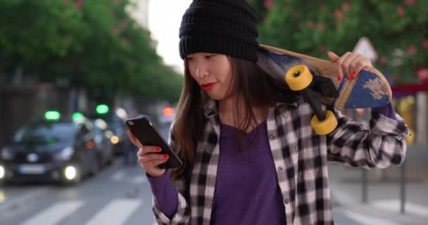 在法国巴黎 希斯特千禧年女人用智能手机和滑板 一个年轻的亚洲女人在城市街道上拿着滑板自拍的画像 — 图库视频影像