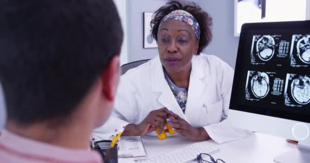 非洲资深医生为患有大脑异常的年轻男性病人开药方 中年黑人医生向年轻病人解释颅内扫描的结果 — 图库视频影像