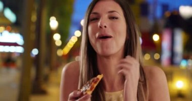 Bin yıllık kızın alışveriş merkezinde gülüp pizza yediği yakın plan. Kahverengi saçlı çekici bir kadın açık hava alışveriş merkezinde pizza yiyor. 4k