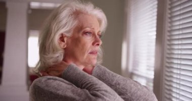 Pencereden dışarı bakan boynu ağrıyan yaşlı bir kadına yakın durun. Kronik boyun ağrısı olan, 50 'li yaşlarda, endişeli görünen olgun bir kadın. 4k