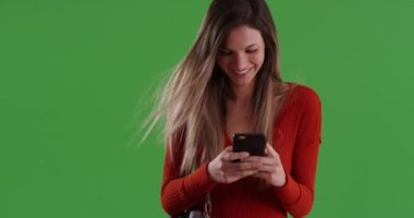 Millennial 'lı kadın, rüzgar saçlarını yeşil ekrana savururken gülümseyip gülerken akıllı telefonuna mesaj atıyor. 20 'li yaşlarda beyaz bir kız cep telefonuyla mutlu mesut mesajlaşıyor. Yeşil arkaplanda 4k