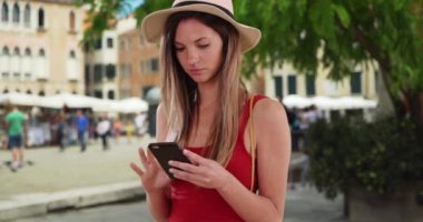 Kırmızı tişörtlü şık bir kadın Venedik, İtalya 'dayken telefonunu kullanıp etrafa bakıyor. 20 'li yaşlarda beyaz bir hippi kız İtalyan şehir ortamında akıllı telefondan mesaj atıyor. 4k