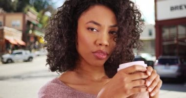 Kahve fincanı tutan güzel Afrikalı kadının kameraya dalgın dalgın baktığı yakın plan. Hoş, küçük bir kasaba ortamında düşünceli bir ifadeyle güzel siyah bir kadının portresi. 4k