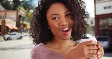 Güzel, siyah bir bayanın kahve içip güldüğü ve kızardığı bir sahne. Çekici, küçük kasaba ortamında kahve içen güzel Afrikalı bir kadının portresi. 4k