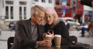 Akıllı telefondan sevimli fotoğraflara bakan gülümseyen bir çift. Açık havada cep telefonu kullanan olgun bir erkek ve kadın. 4k