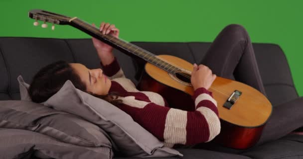 可爱的拉丁女性的肖像躺在沙发上 弹吉他 在绿色的屏幕上微笑 在绿色屏幕上键入或合成 — 图库视频影像
