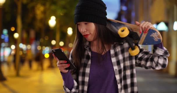 スマートフォン上のヒップスター千年紀の女性ネットワークとシャンゼリゼパリフランスでスケートボードを運ぶ 都会の中でスケートボードを持って自撮りした若いアジアの女性の肖像画 — ストック動画