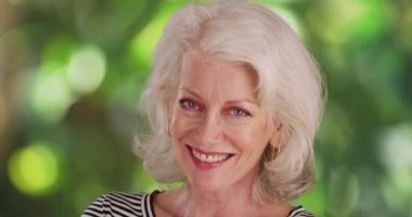 Kameraya gülen mavi gözlü, sevimli son sınıf kadınını yakından çek. Kameraya gülümseyen, arka planda sallanan ağaçlar olan neşeli yaşlı kadının yakın çekimi. 4k