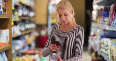 Marketteki kadın akıllı telefondan beslenme bilgilerine bakıyor. Annem teknolojiyi kullanarak süpermarketten alışveriş yapıyor. 4k