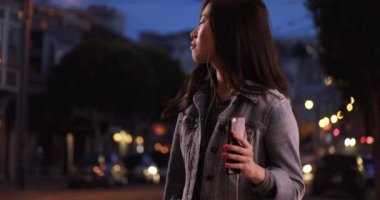 Milenyum kadını müzik dinlemek için akıllı telefon kullanıyor ve gece San Francisco 'da kot ceket giyiyor. Şehir caddesinde dans eden sevimli Asyalı kadının yakın çekimi. 4k