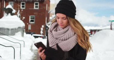 Çekici milenyum kızı, karda küçük bir kasabada akıllı telefondan mesaj atmak için eldivenlerini çıkarıyor. Genç beyaz kadın dışarıda, karda cep telefonuyla mesajlaşıyor. 4k