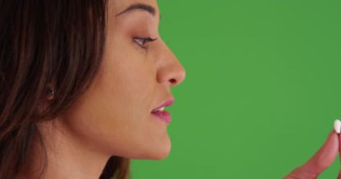 Genç Latin bir kadının hap içip yeşil ekranda su içtiği yakın plan. Anahtar ya da birleşik olmak üzere yeşil ekranda.