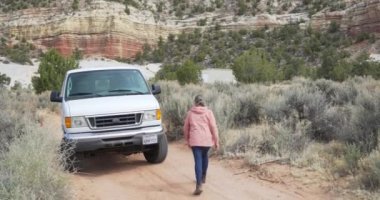 Doğal parktaki toprak yolda büyük bir minibüs kullanan bağımsız bir yaşlı kadın. Dışarıdaki yaşlı kadın doğada büyük boy bir aracı hareket ettiriyor.