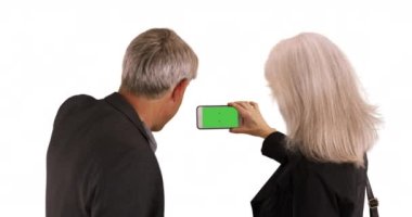 Yaşlı çift beyaz arka planda fotoğraf çekmek için akıllı telefon kullanıyor. Yeşil ekranlı akıllı telefon taşıyan yaşlılar. 4k