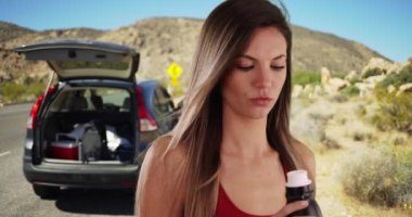 Kırmızı elbiseli bir kadının yol gezisi sırasında çölde şişeden su içmesi. 20 'li yaşlarındaki sağlıklı beyaz kız çölde su şişesinden araba içiyor. 4k