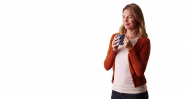 Orta yaşlı, beyaz arka planda kahve fincanından gülümseyen ve içen beyaz bir kadın. Çekici beyaz kadın sıcak içecekten zevk alıyor ve stüdyoda fotokopi odasıyla gülüyor. 4k