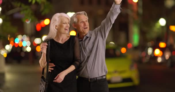 夜に屋外に立つシニアカップルはタクシーを利用しようとする 高齢者のカップルに乗るのを待っている — ストック動画